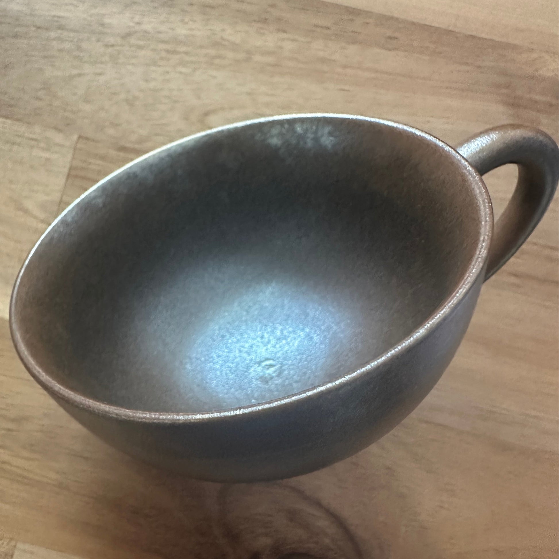 Bronze-colored wood-fired ceramic latte coffee tea cup on a wooden surface