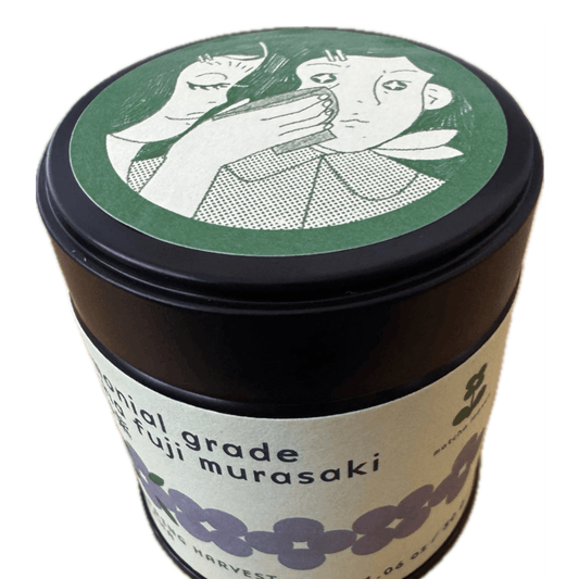 Matcha tin canister with decorative lid featuring illustrations of a woman and a child