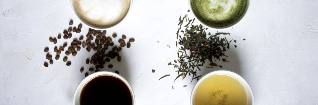 Top view of four cups of coffee latte, matcha latte, black tea and green tea in a square order with some coffee beans and loose leaf tea in the middle - café la maison J.