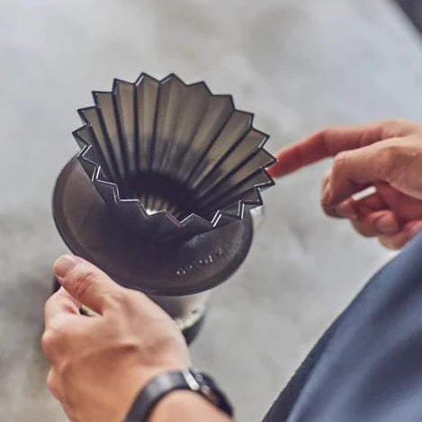 A man looking at a glass coffee server with a black AS resin ORIGAMI Dripper Holder and black ORIGAM AS resin coffer dripper on it