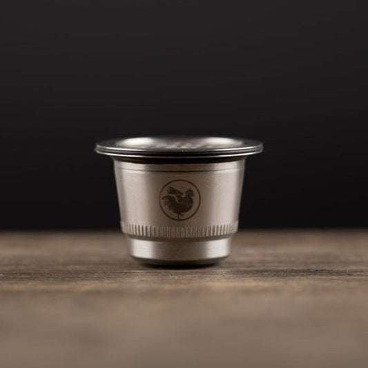 a WAPCAP stainless steel coffee pod for Nespresso  on a grey surface and black back drop