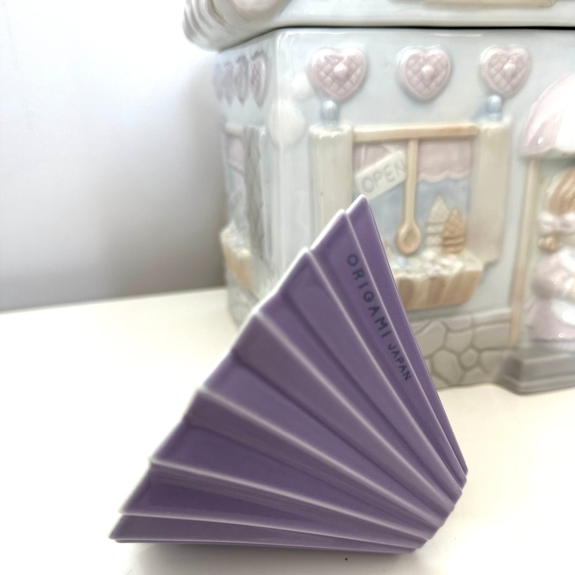 A purple ORIGAMI Coffee Dripper M, there is " ORIGAMI Japan" showed on the rib, and there is a house cookie jar at the back 