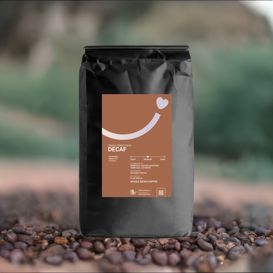 A bag of organic single origin Peru Decaf coffee with surrounded by roasted coffee beans and blur green mountain background
