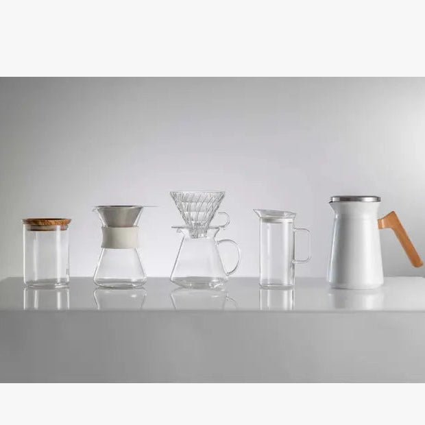 Set of glass and metal coffee brewing equipment on a white surface with a light gray background