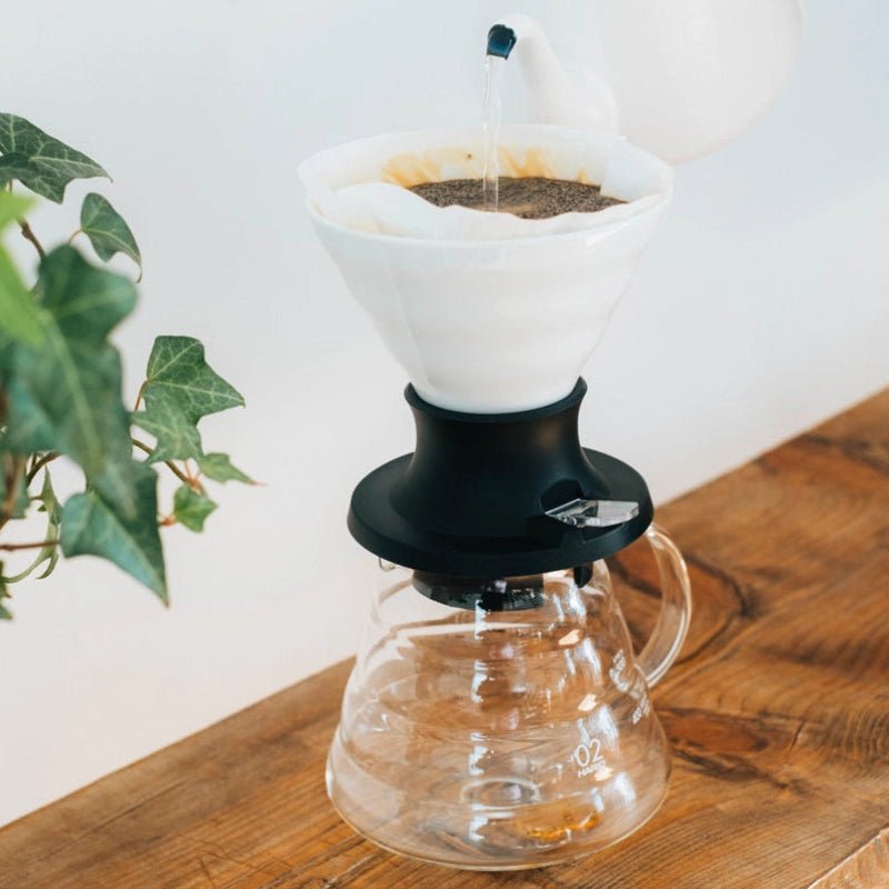Coffee brewing setup with a white ceramic dripper, switch and clear carafe on a wooden surface.