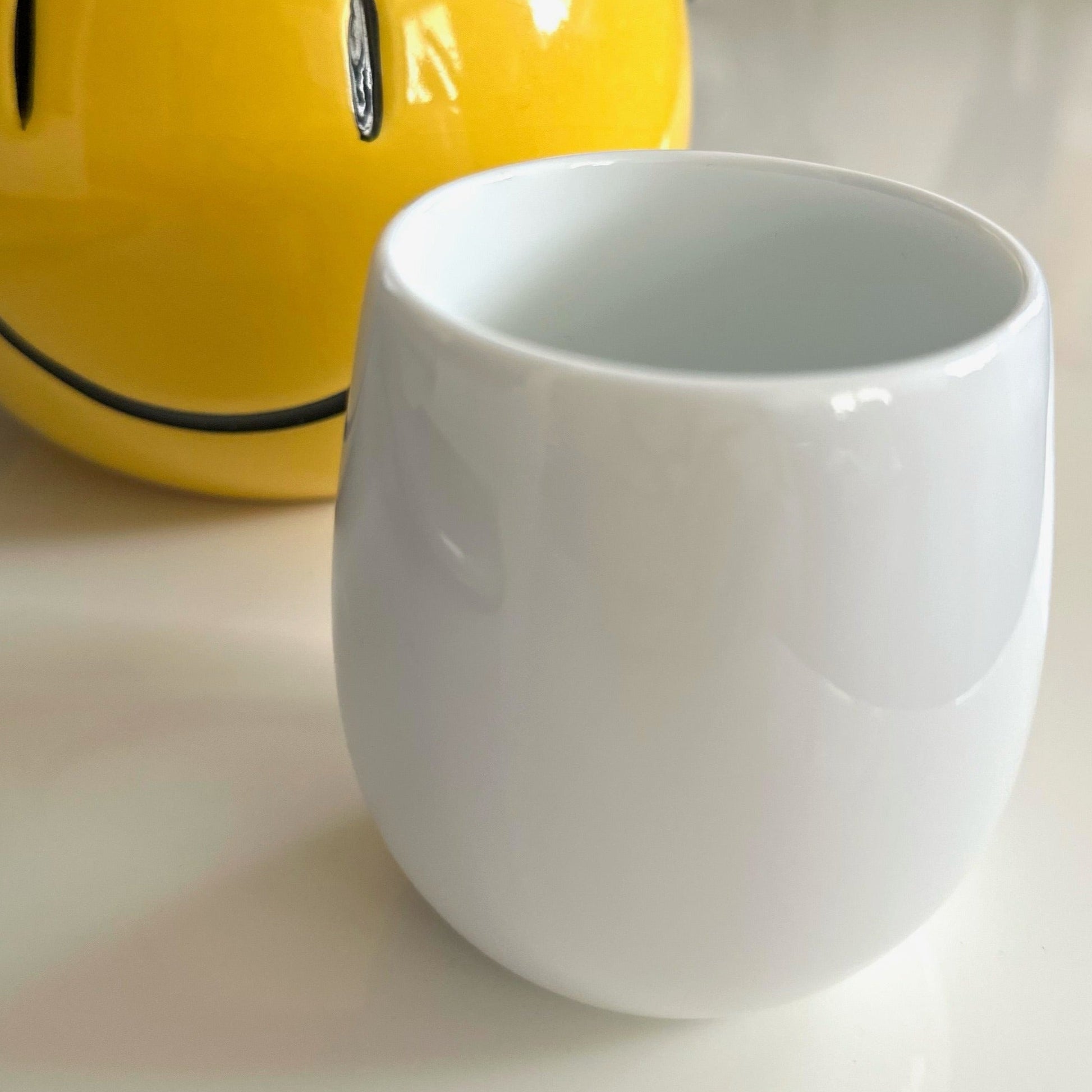 Front is a  white porcelain ORIGAMI Barrel Flavor Cup, at the back is a round shaped happy face vase 