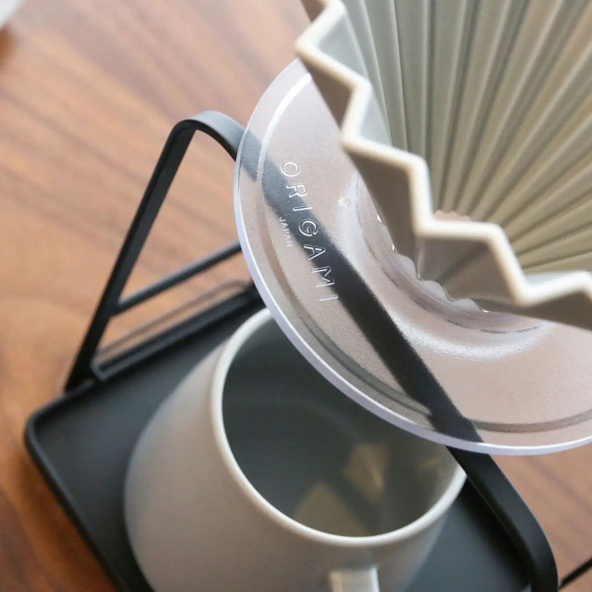 A gray Origami ceramic coffee filter on a clear plastic dripper holder and ceramic carafe with a wooden surface in the background