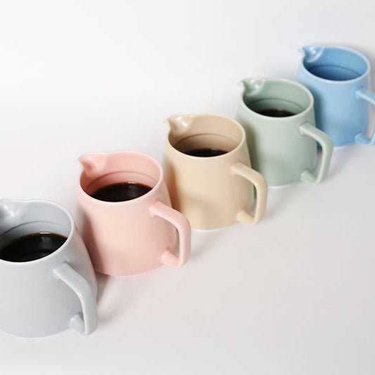 Set of matte colors ceramic servers with coffee on a light background